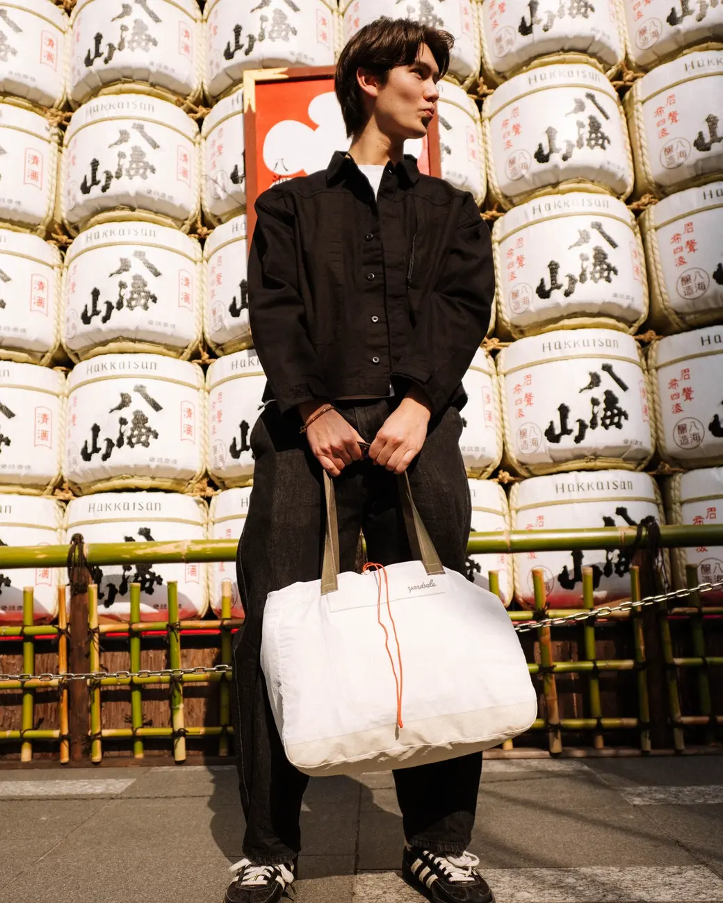 A man holding a 20L Day Bag in Tokyo in front of sake barrels